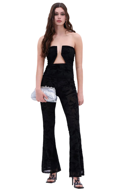 Woman wearing a black strapless top and flared pants with a silver clutch on a white background