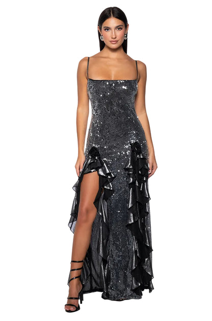 Woman wearing a sparkly black evening gown with a high slit on a white background