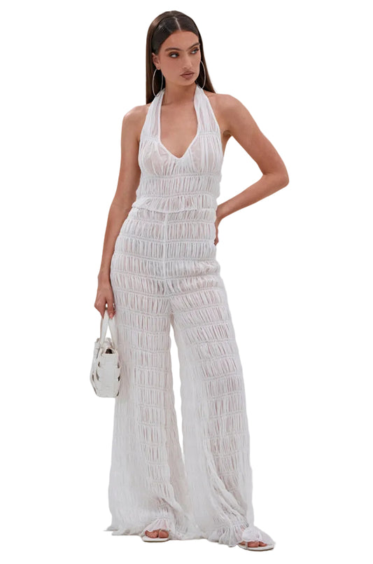 Woman wearing a white smocked jumpsuit on a plain background